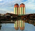 cities INDONESIA Jakarta. Man in a wooden boat navigating a polluted waterway backed by wooden slum housing, in contrast to the high rise appartment buildings visible behind.
Credit: Mark Henley / Panos.