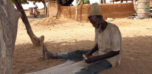 Man in a village in Ghana making a new fishing net