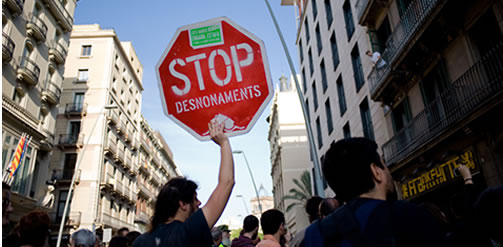 An 'Indignado holding a placard that reads -stop evictions- in front of a bank (May 2012). Several groups of 'Indignados' perform actions against banks in Barcelona due to evictions because of crisis. Credit. Jordi Boixareu - Flickr CC BY-NC-ND 2.0