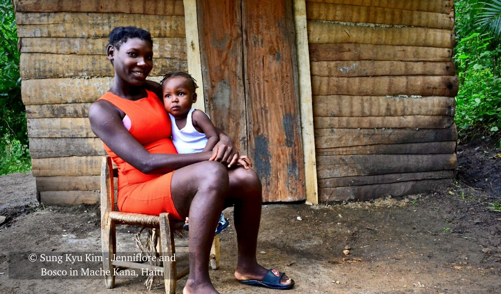 Jenniflore holds her son Bosco on her lap outside their home in Mache Kana, Haiti