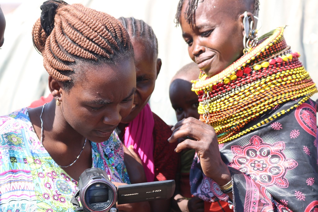 Three women look at a video cameria. Sarima residents review video material they have generated as part of the ‘Seeing Conflict at the Margins’ project. 
