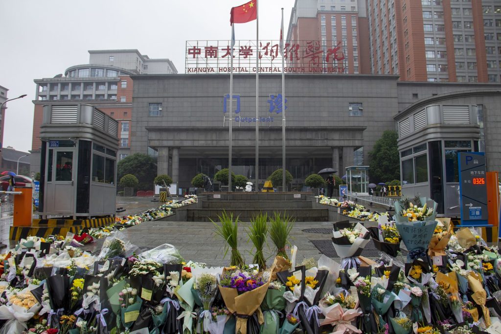 Hundreds of bunches of flowers outside Xiangya Hospital after the death of Yuan Longping. The Chinese flag flies at the front of the hospital and there is a large red sign with the name of the hospital.