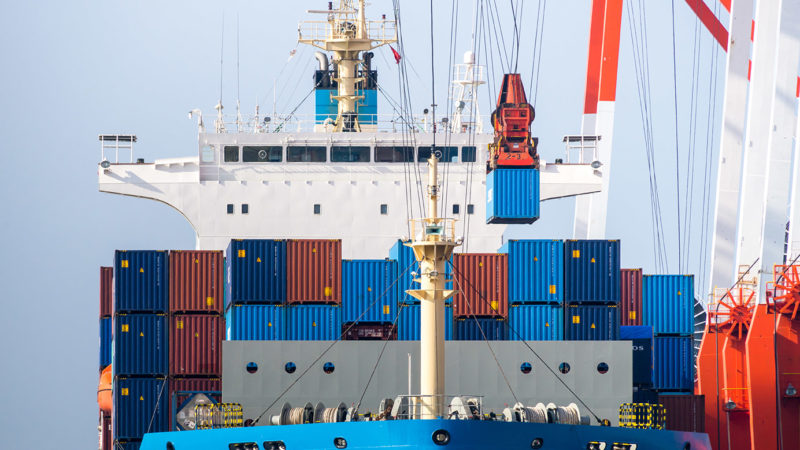 Container ship with colourful containers and port cranes next to it.