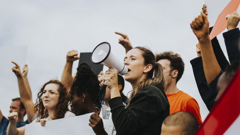 Woman holding megaphone in a group of activists protesting.