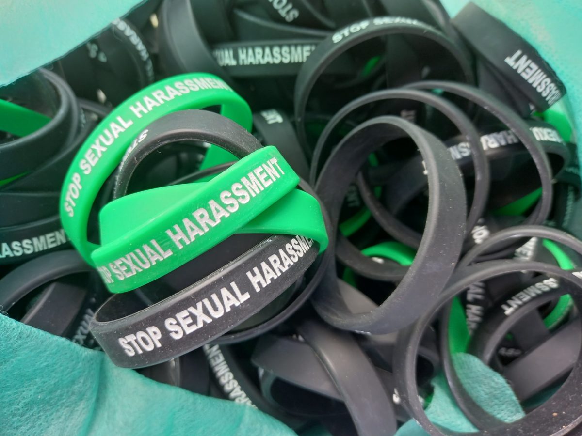 A collection of green and black plastic bracelets saying 'stop sexual harassment'