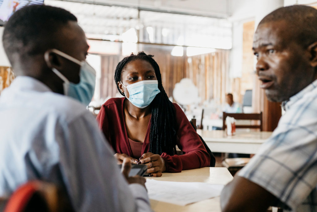 A woman from Mozambique is wearing a facemask, either side of her are two men. They are sitting in an office.