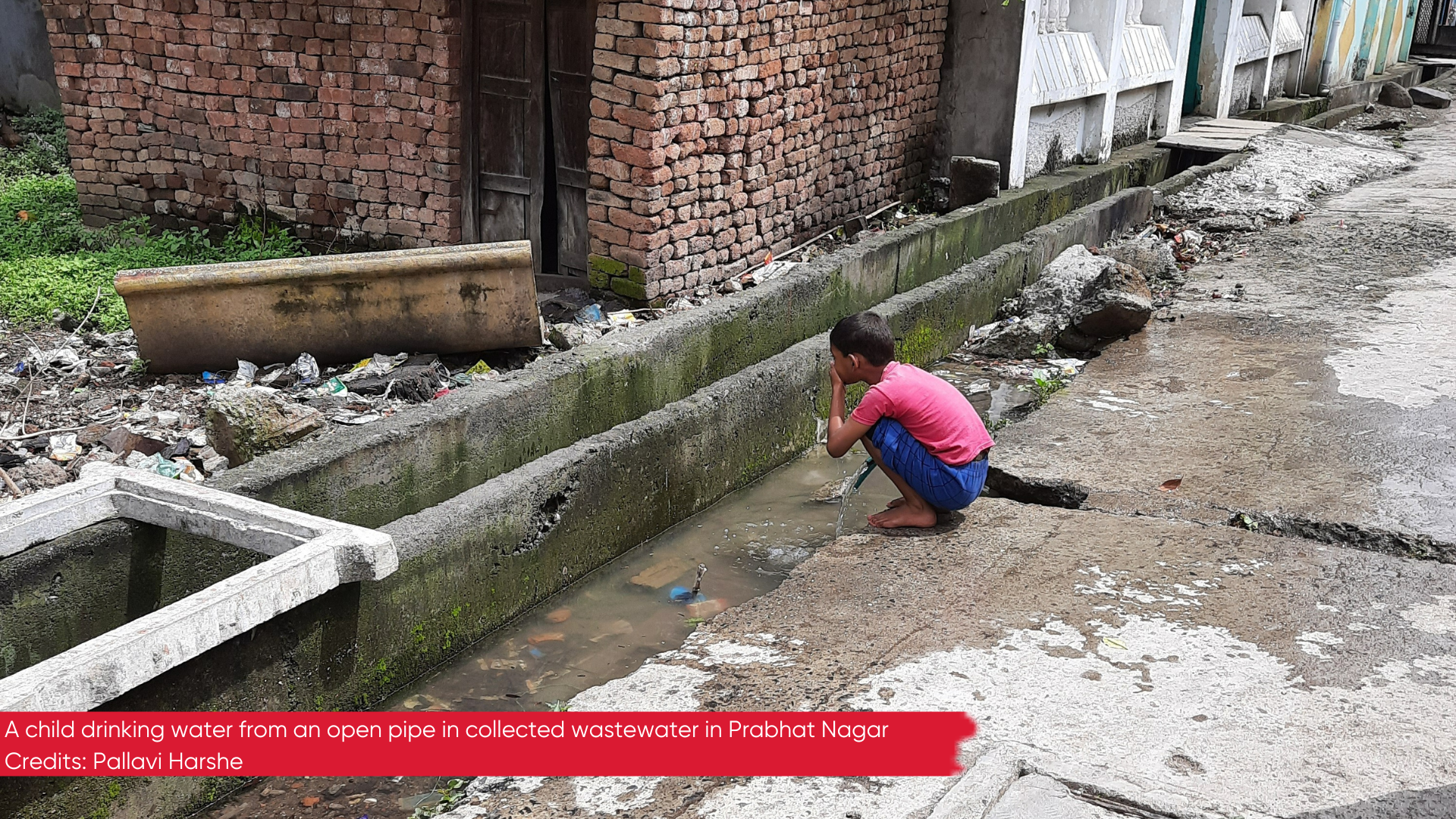 Photo of a child drinking water from an open pipe located in collected wastewater in Prabhat Nagar