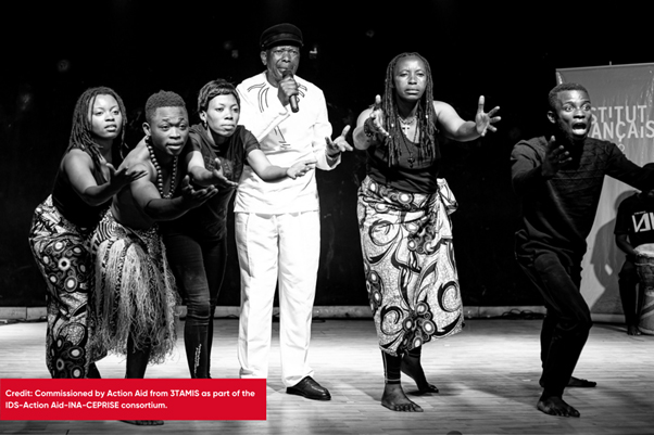 A singer from the DRC is flanked by 5 dancers. They are dressed in traditional DRC clothing.