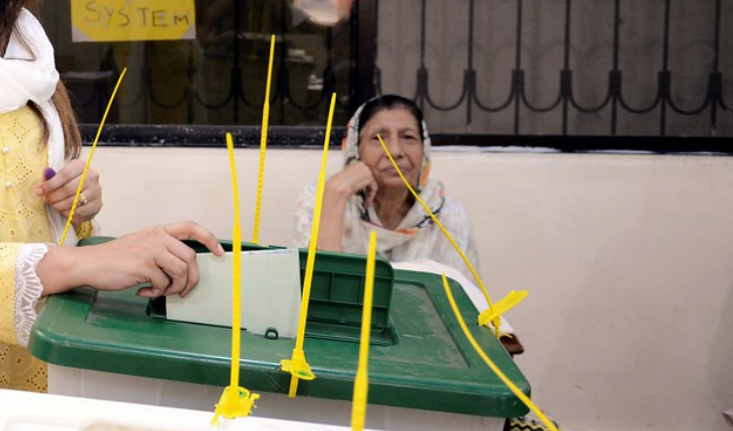 A person, mostly unseen except for their hand, drops a piece of paper into a ballot box.