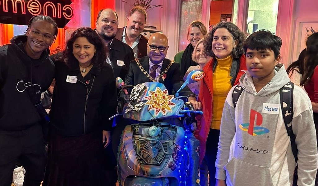 A group of people smiling and looking at the camera, standing around a brightly decorated moped