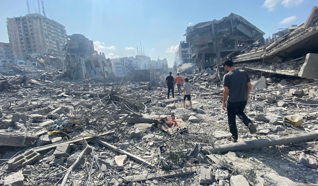 Palestinian men walking over rubble of a bombed out building, inspecting the damage following an Israeli airstrike.