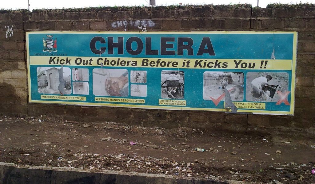 A sign on an outdoor wall saying 'kick out Cholera or it will kick you'.