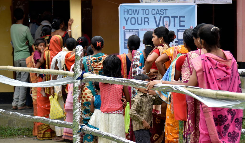 Voters stand in a queue to cast their votes at a polling station for by-polls under Jania constituency in Barpeta district of Assam.