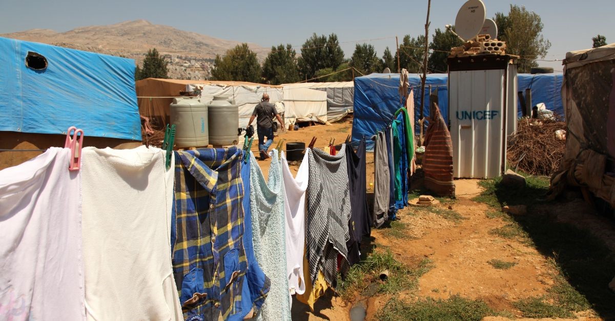 A line of washing drying in the sun in a refugee camp, with temporary buildings branded with a Unicef sign in the background.