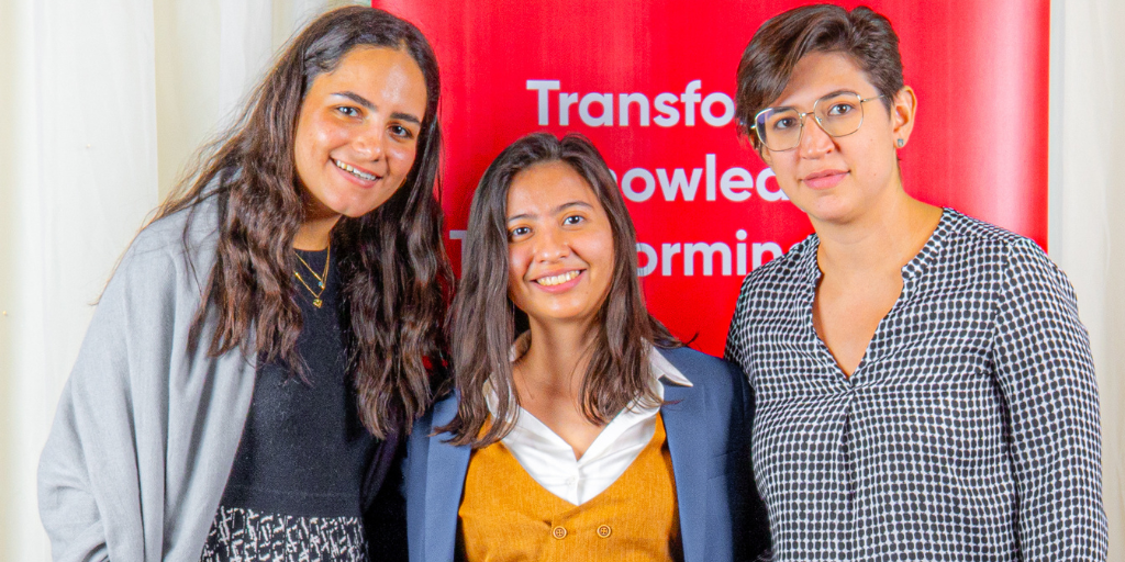 Three women standing infront of a red banner.