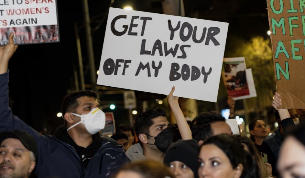 People in a crowded demonstration, with one holding up a homemade banner reading 'Get your laws off my body'.