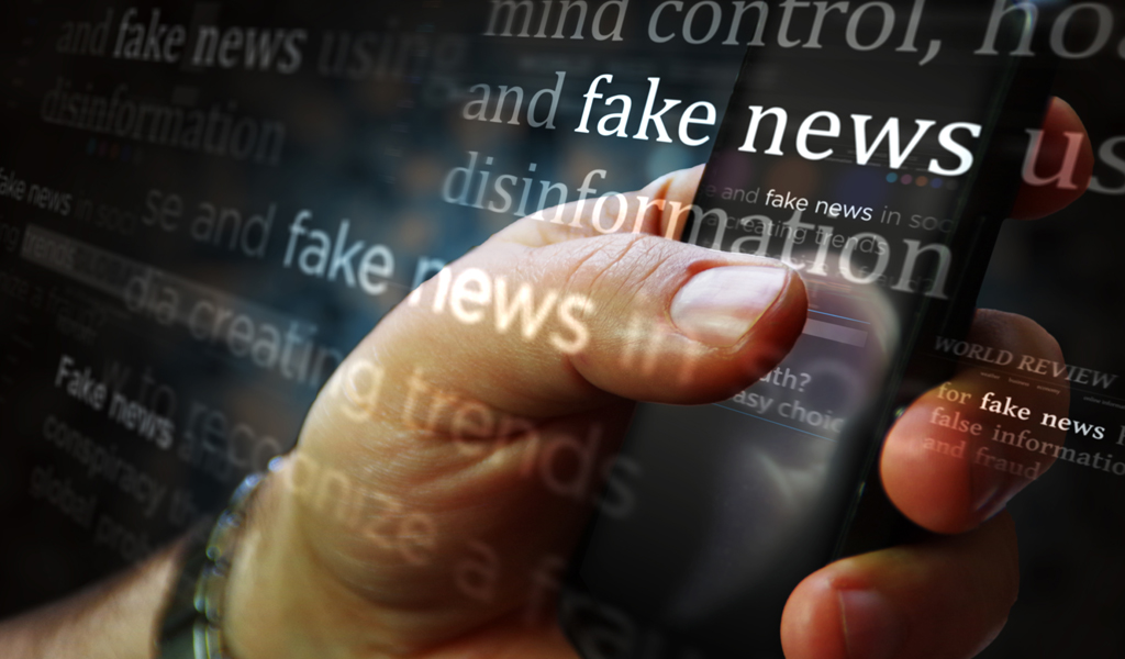 A hand holds a phone with fake news and disinformation overlay-ed on the image