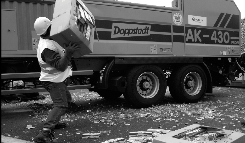 Man in protective gear throwing a box full of smuggled Malboro cigarettes in a shredding truck to destroy them.