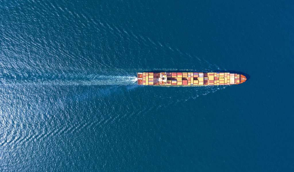 Overhead view of a long narrow tanker ship travelling over a calm, deep blue sea.