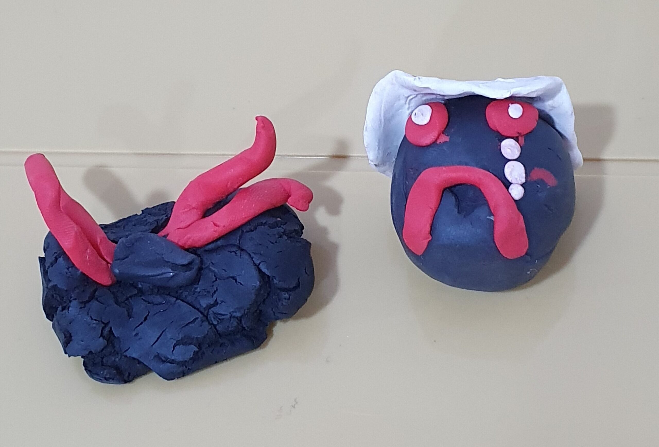 Two plasticine models: one is a blue, crying face with a white hat. The other is a blue camera.