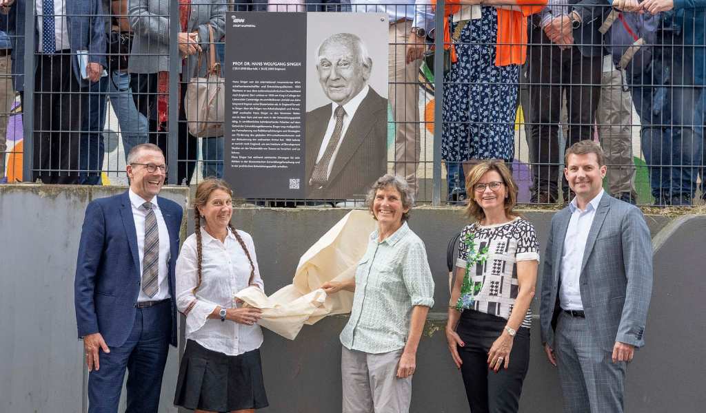 A group of people standing either side of a commemorative sign with text and a black and white photo of Hans Singer.