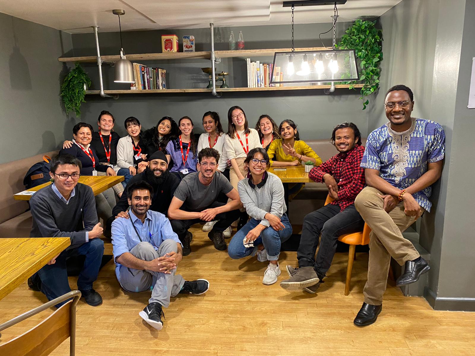 A group of masters students in a cafe sit together for a photo.