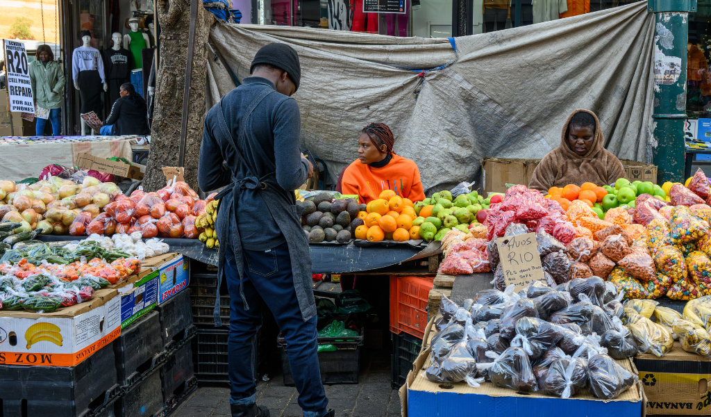Woman sitting at a stall selling different fruits and vegetables.