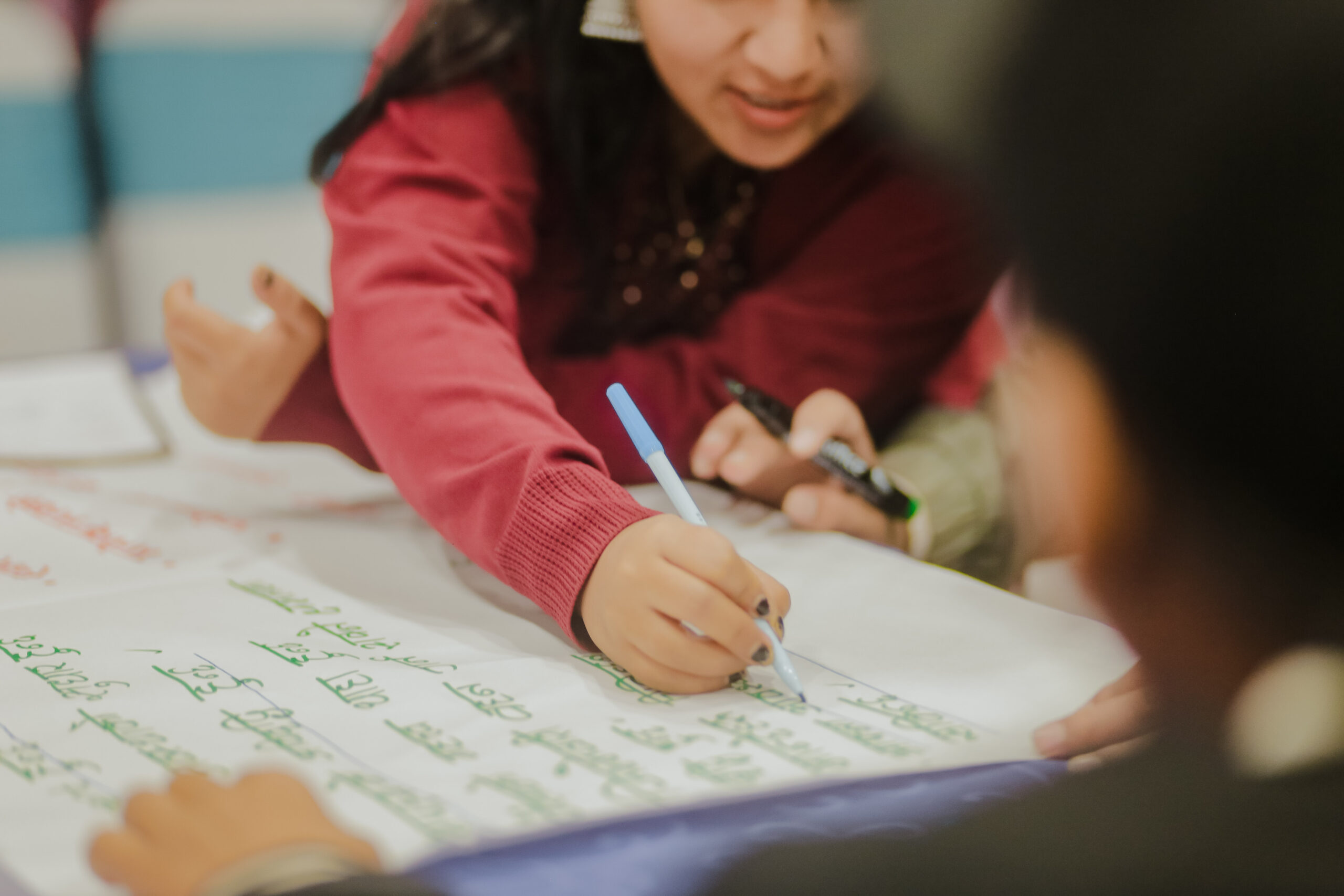 A girl with long dark hair in a pink long-sleeved top leans over to write on a flip chart .