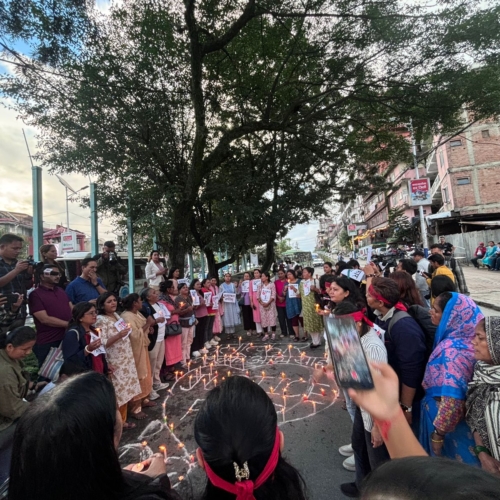 A group of people stand outside under a tree in a circle. Inside the circle are candles arranged ina heart shape with the word &#039;justice&#039; in the centre.