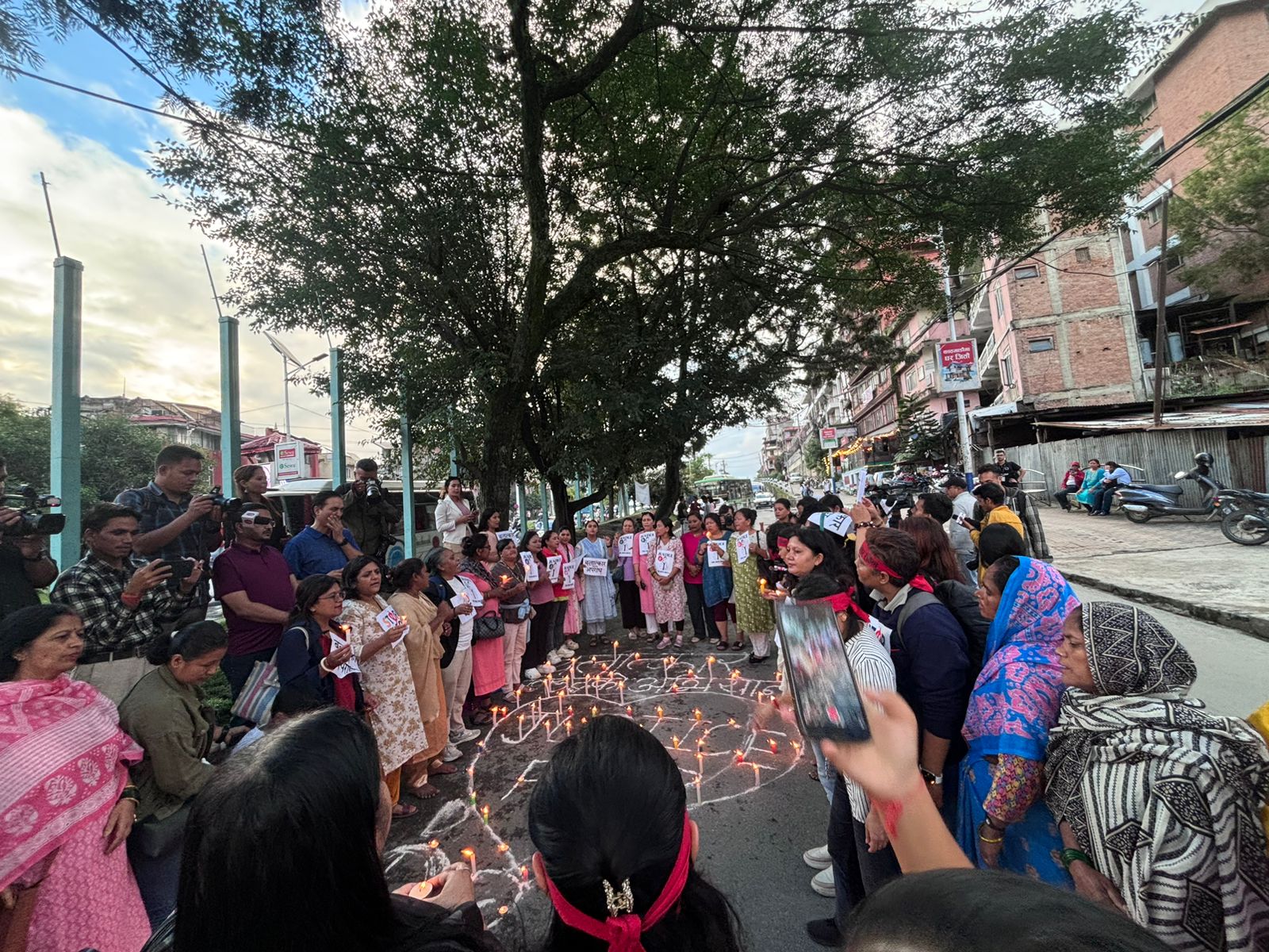 A group of people stand outside under a tree in a circle. Inside the circle are candles arranged ina heart shape with the word 'justice' in the centre.