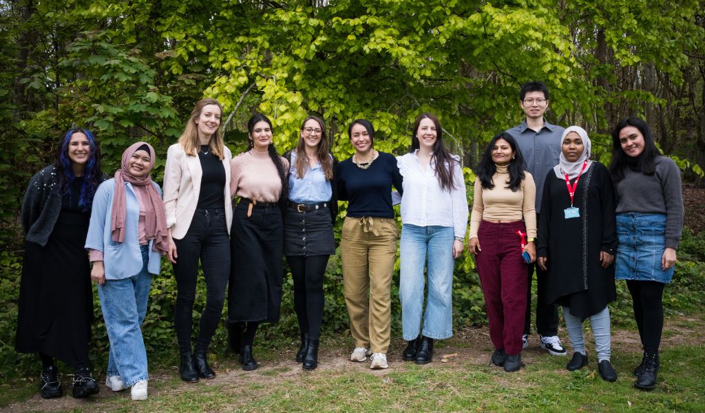 Eleven PhD researchers stand in a line smiling at the camera. They are a selection of genders and nationalities.