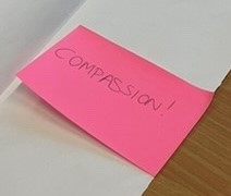 A pink Post-It note stuck to flipchart paper reads 'Compassion', followed by an exclamation mark.