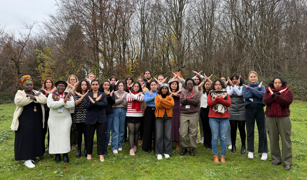 A group of IDS students stand outside on the grass with trees in the background with their arms are crossed in front of their chests.