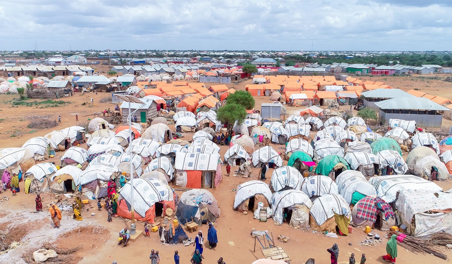 A collection of roughly built shelters in the foreground, with huts with orange roofs in the background.