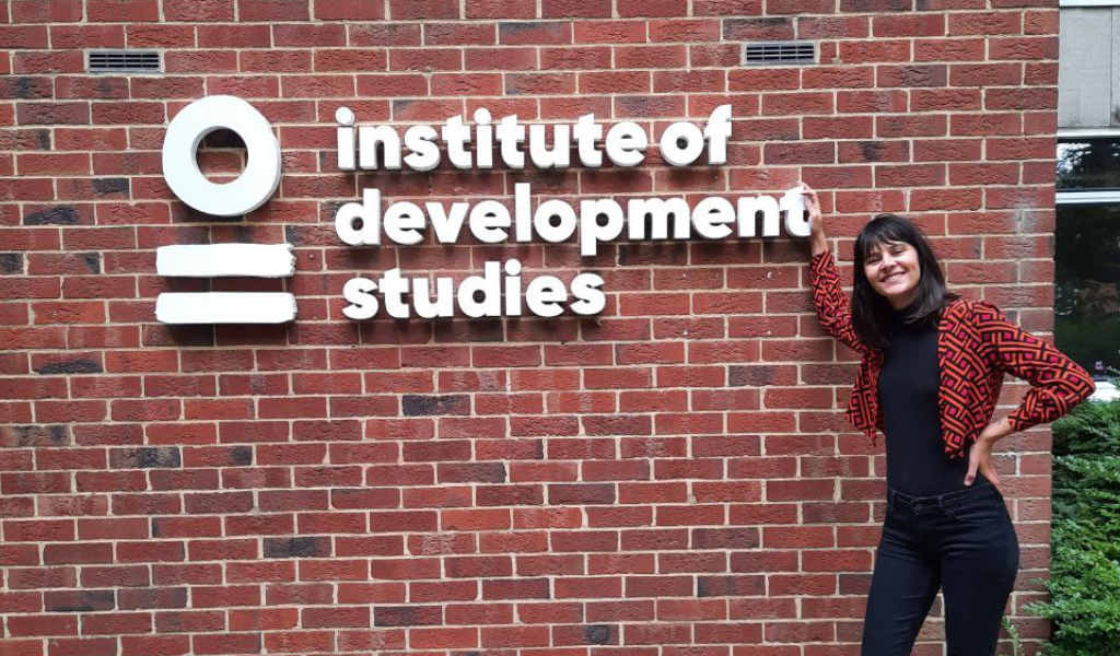 A woman stands in front of a red brick wall next to a sign saying 'Institute of Development Studies'.