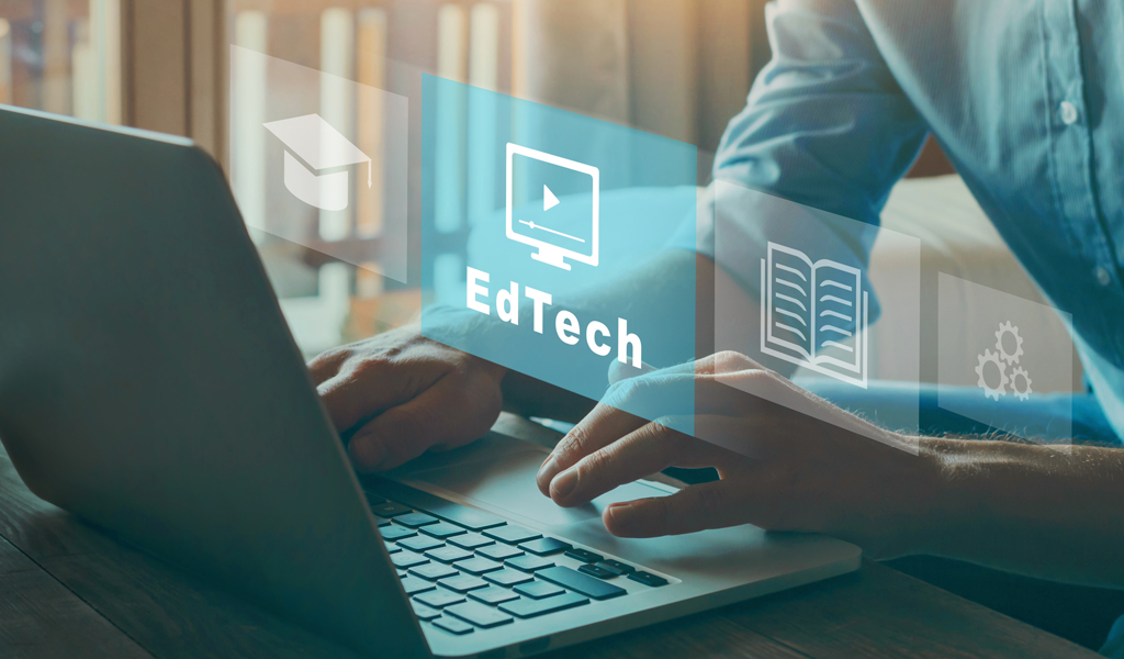 This is a photo of a woman typing on a laptop. We cannot see her face but superimposed is the word EdTech in a blue transparent box.