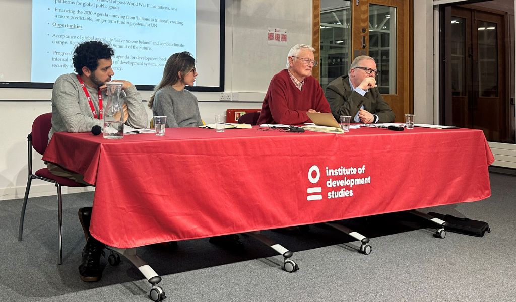 A photo of four people sat behind a table, which is covered in a red table cloth with the IDS logo in white at the front.