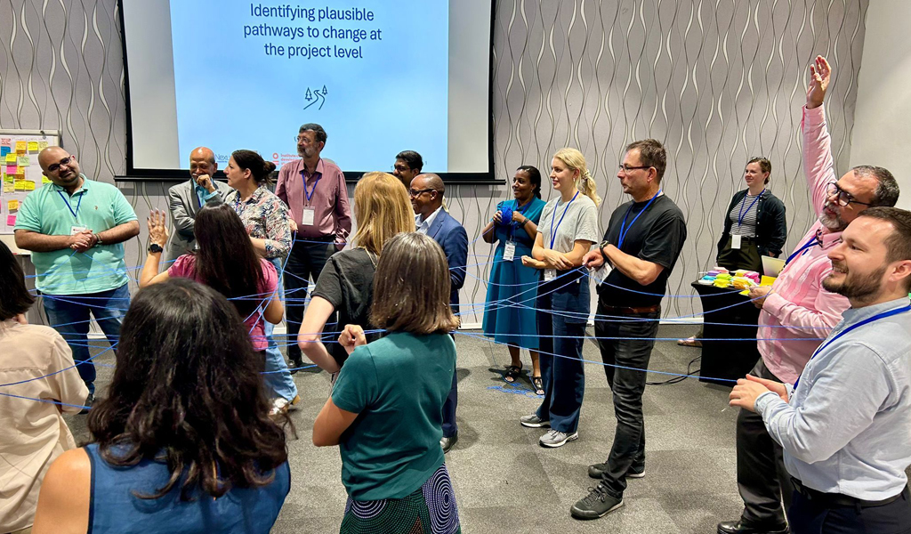 A photo of a group of participants standing around each other all holding a long piece of string.