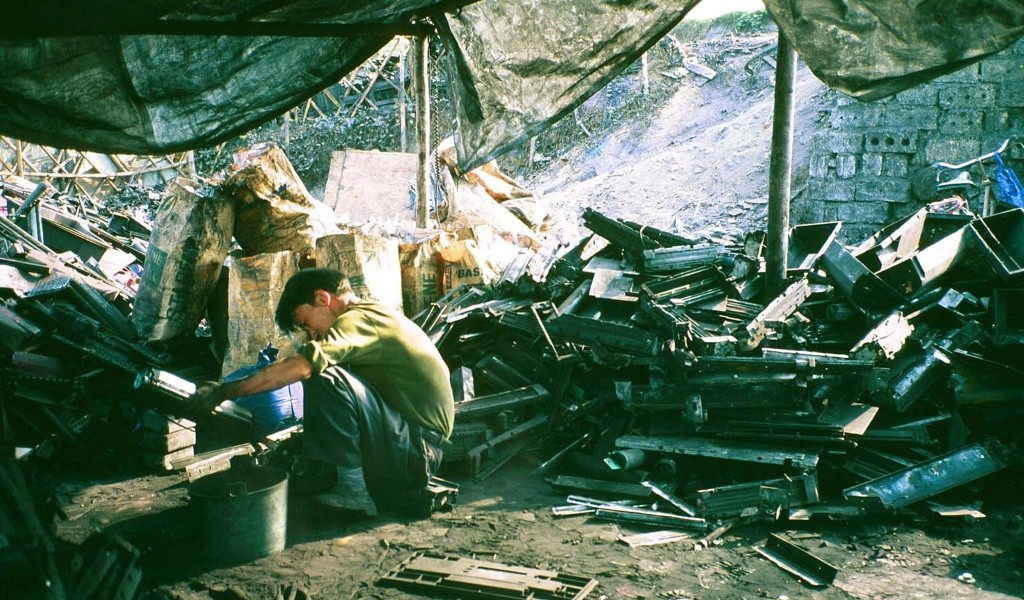 A man crouches down, surrounded by old pieces of computer equipment. He looks to be cleaning one of the pieces of equipment.