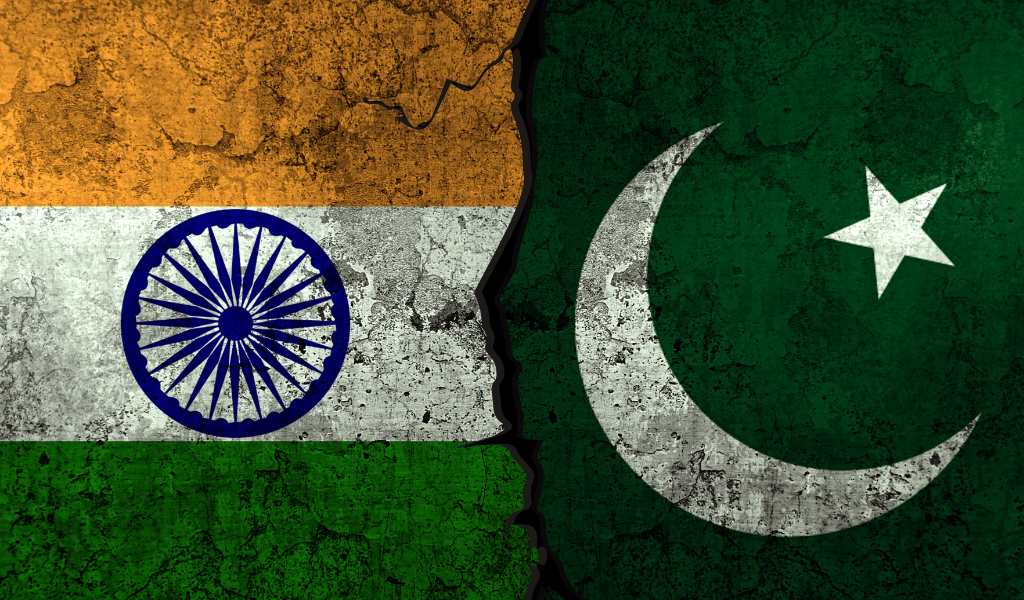 A worn India country flag with orange, white and green horizontal stripes with a blue wheel in the centre on the left hand with a worn Pakistan flag on the right. The Pakistan flag is dark green with a thin white moon and star.