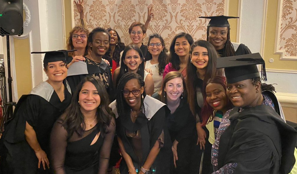 A diverse group of smiling students wearing graduation caps and gowns stand in a group to pose for a picture.