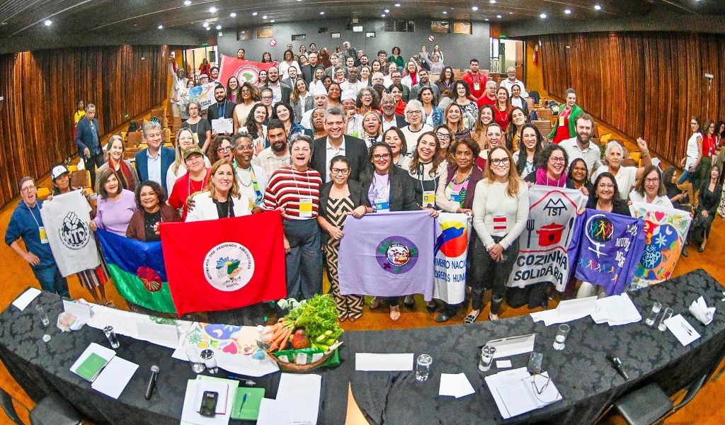 A crowd of people holding flags and banners, inside a packed room and all facing the camera