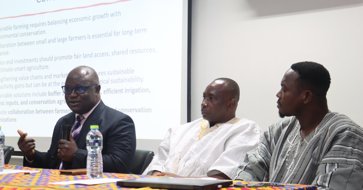 Three men from Ghana sitting at a table with a water bottle on a mustard colour table cloth