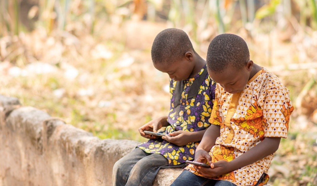 Two children sitting outside play on their mobile phones