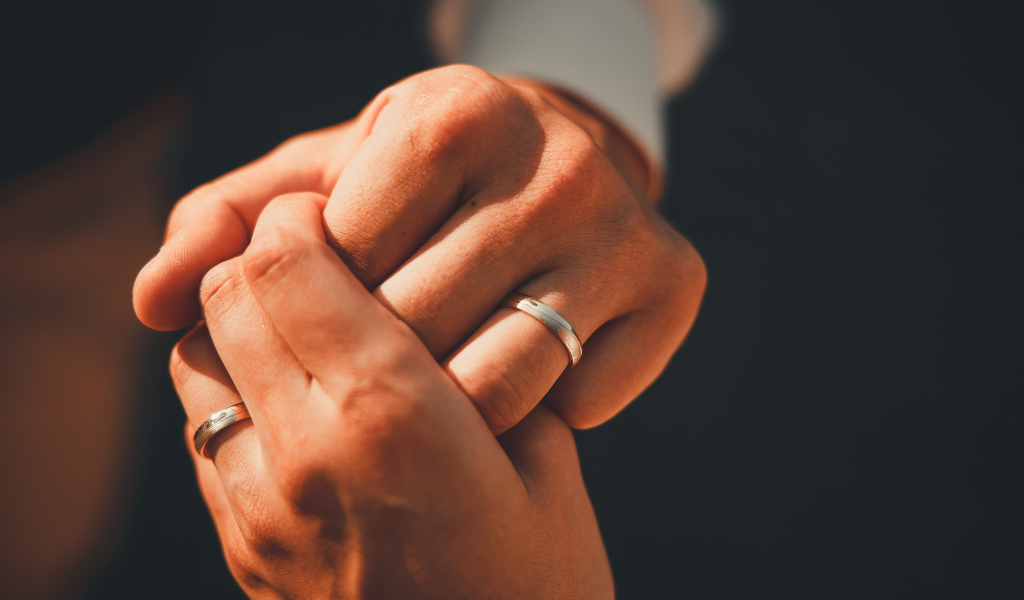 Hands holding eachother with wedding rings on dark background.
