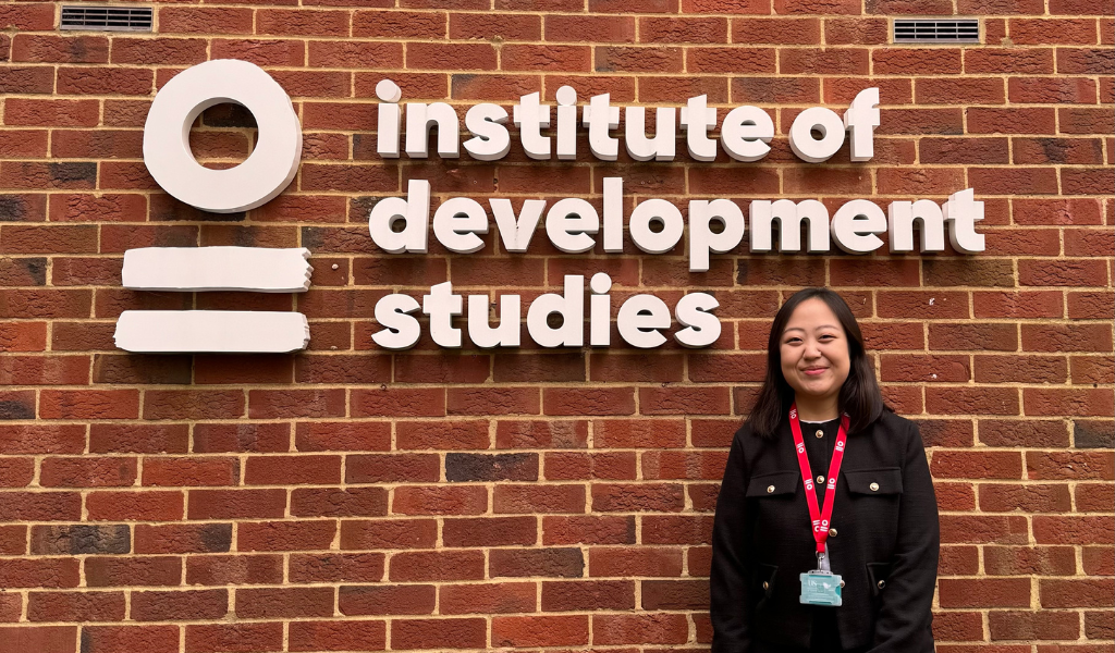 A female wearing all black standing in front of institute of development studies logo and smiling for the camera.