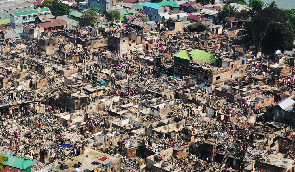 A bird's eye view of a burned out informal settlement in Dhala, Bangladesh. There are burned concrete walls with no roofs.
