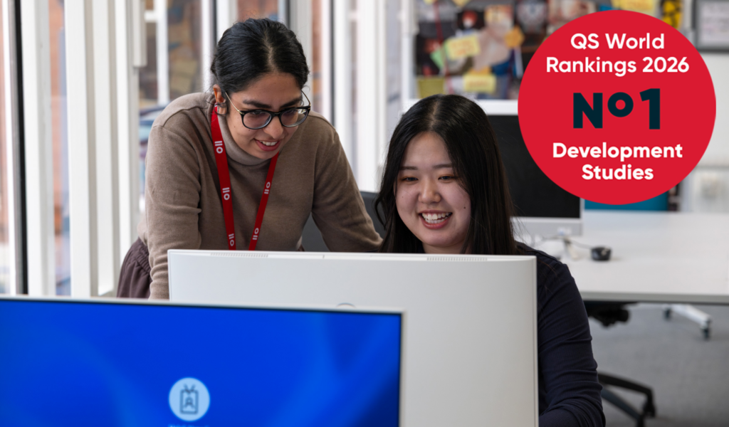 Two students working together at a desktop computer in a bright study space, with a circular graphic reading “QS World Rankings 2026 – No. 1 Development Studies” displayed in the corner.