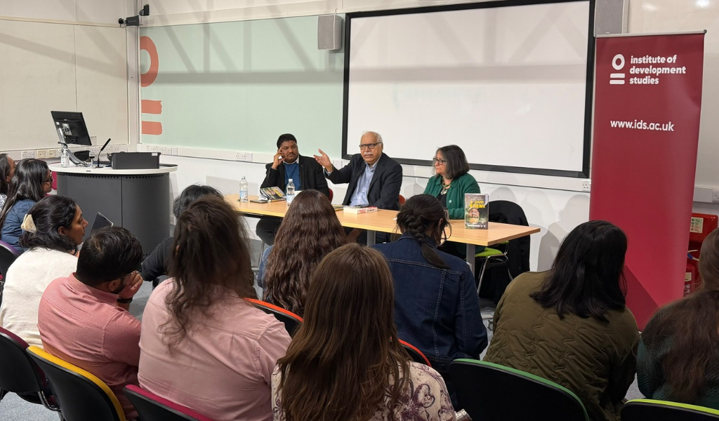 Three people on the panel giving a talk to the audience wsith a white background. Two are men and one is a woman.